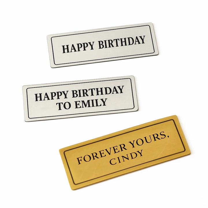 Brushed gold and polished silver plaques with phrases like “Happy Birthday” and “Forever Yours”