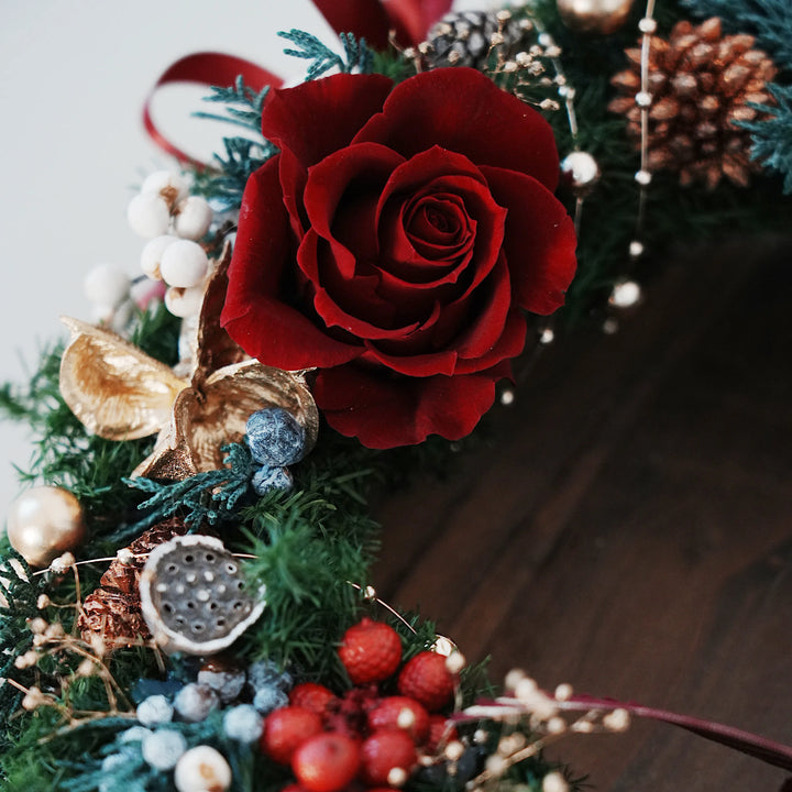 Decorative wreath with red everlasting roses, pinecones, and berries 