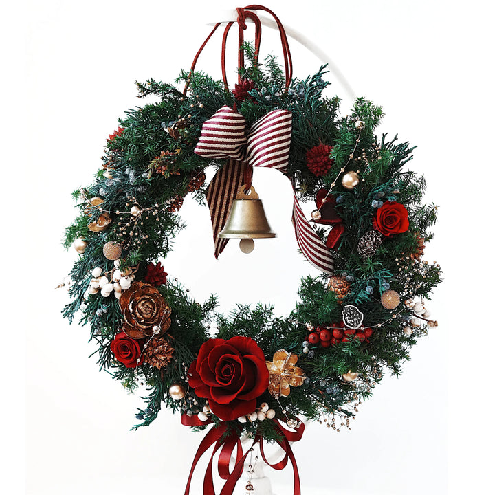 Large everlasting Christmas wreath handcrafted with preserved red roses, pine foliage, and gold ornaments, featuring a striped ribbon bow and golden bell on a white background
