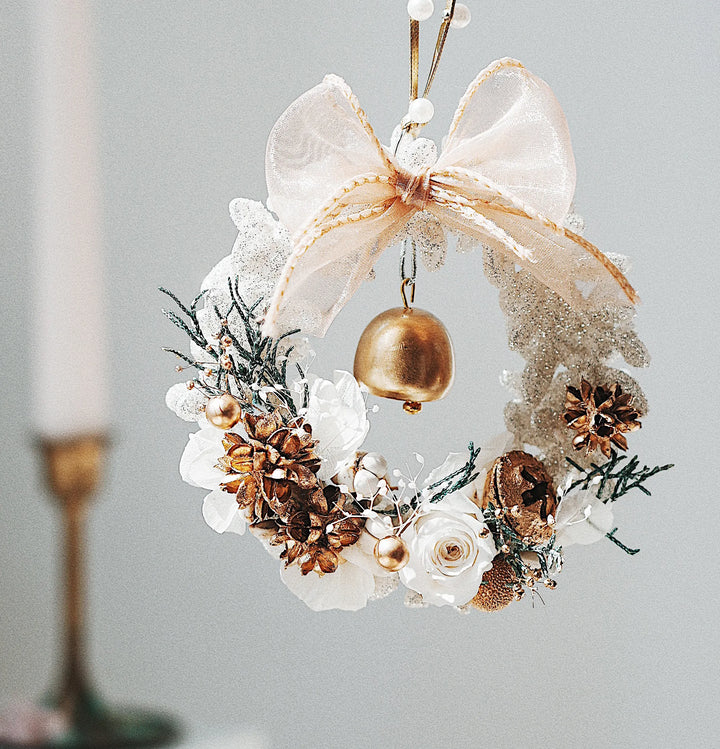 Everlasting Christmas wreath with preserved flowers, golden bell, and sheer ribbon bow in a soft neutral tone, hanging against a light background