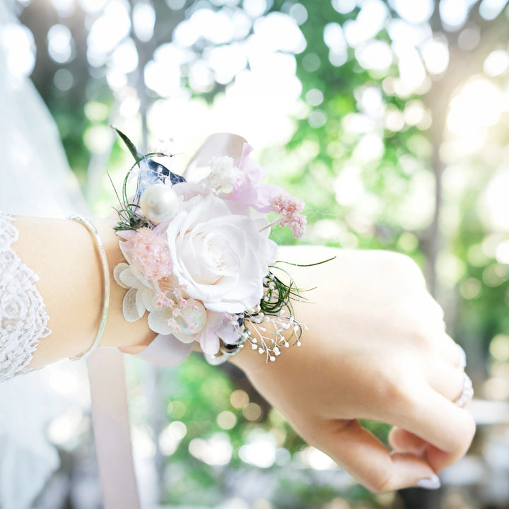 Preserved flower wrist corsage with white rose and pink accents, worn by bride in natural sunlight
