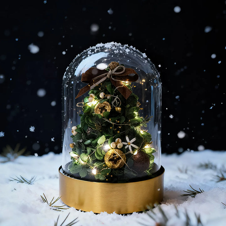 Everlasting Christmas tree in classic green under a glass dome with warm LED lights, set against a snowy dark background