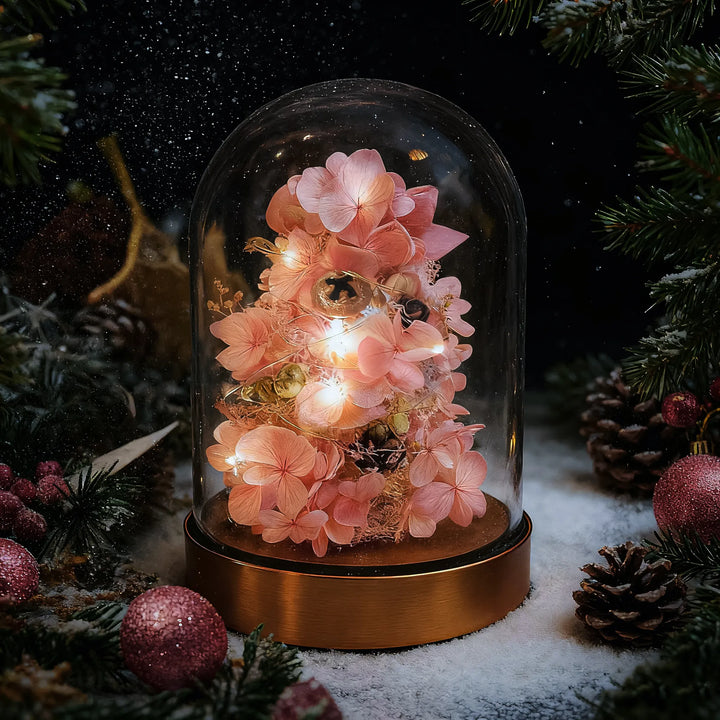 Everlasting Christmas tree in soft pink made with preserved hydrangeas, glowing under a glass dome with warm lights and a festive background