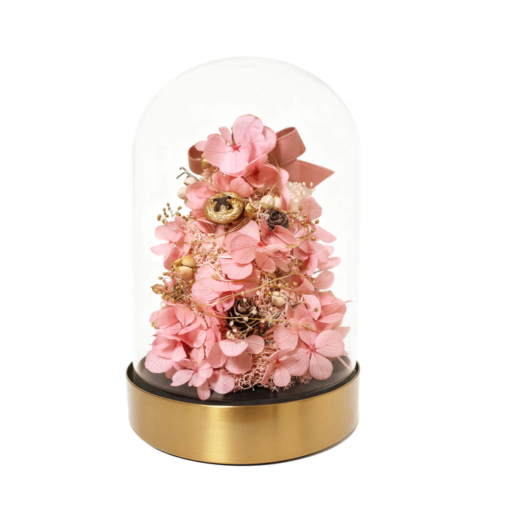Decorative flower arrangement under a glass dome on a gold base with a white background